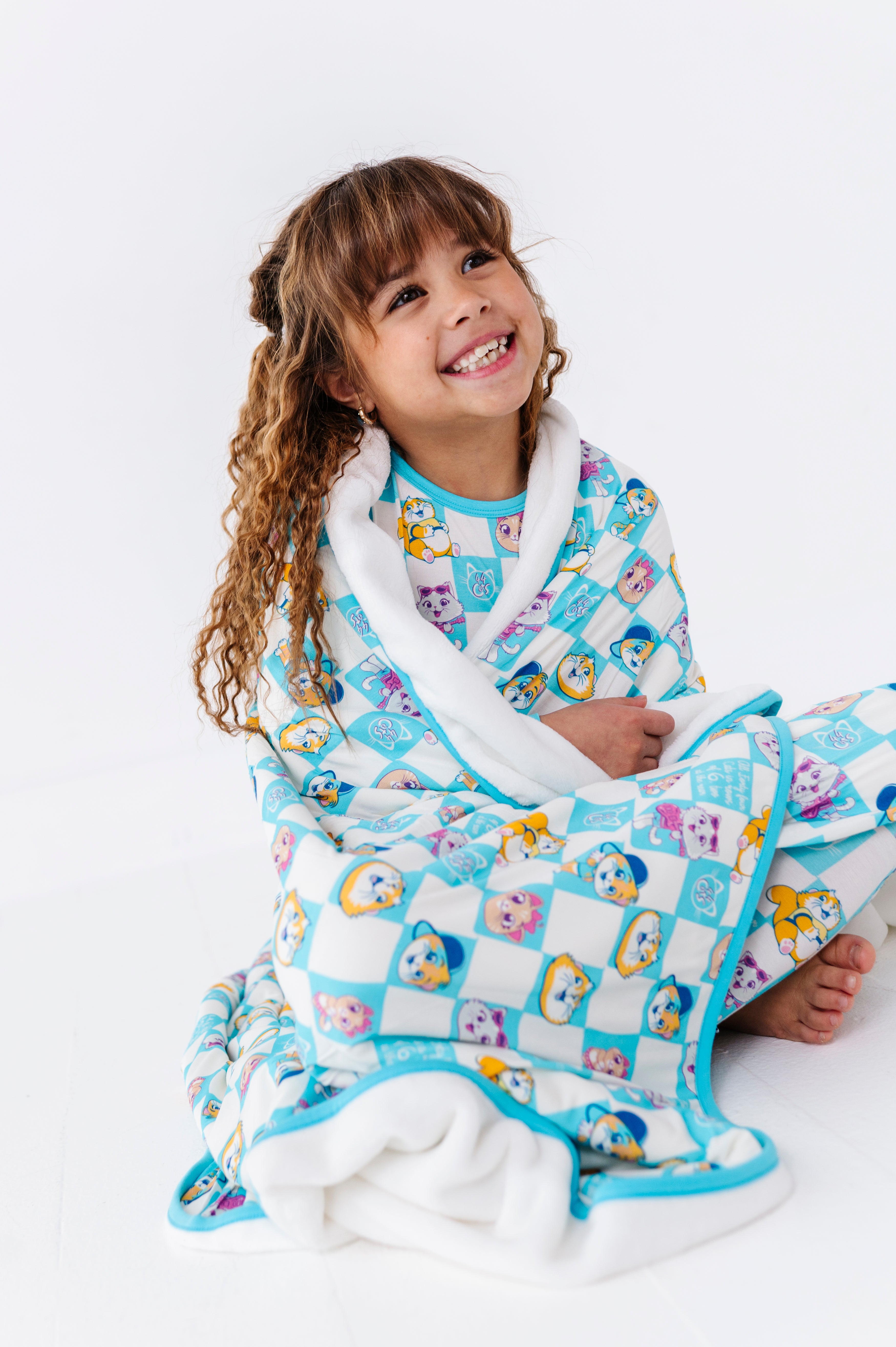 Child wrapped in a colorful 44 Cats bamboo plush blanket on a white background